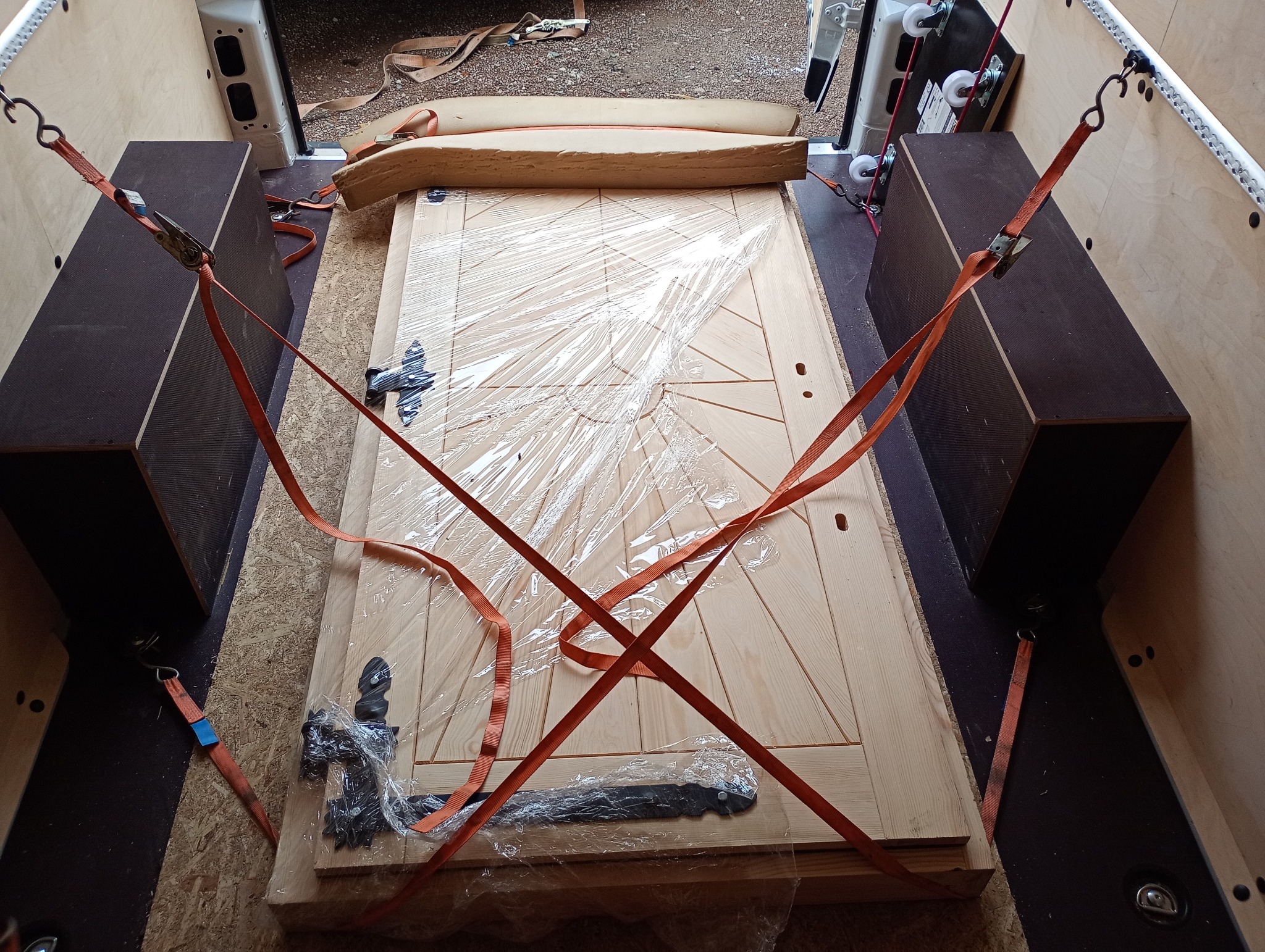 Drzwi z okuciami zabezpieczone pasami wewnątrz pojazdu transportowego, owinięte folią dla ochrony podczas przewozu. Widok z góry.