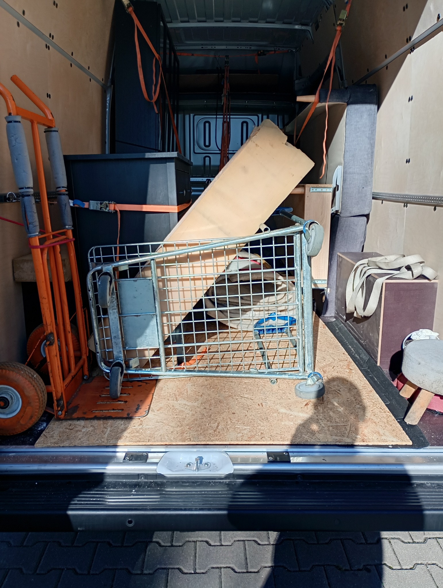 Wnętrze busa wypełnione meblami i sprzętem do transportu, zabezpieczone pasami. Widoczny wózek transportowy i karton. Gotowość do przeprowadzki.