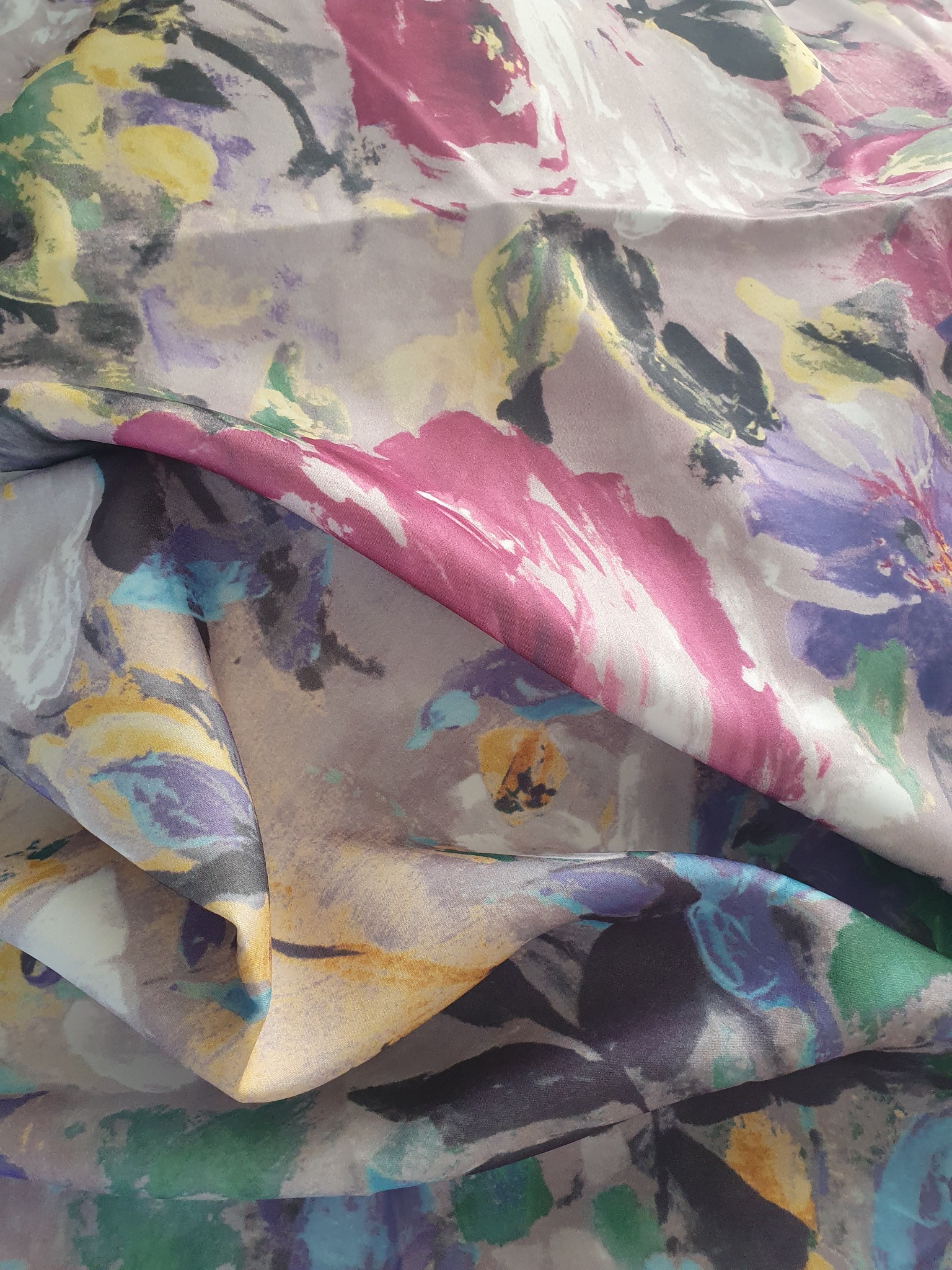 Fałdy satynowej tkaniny w pastelowe kwiaty z przewagą różu, fioletu i zieleni, wzór przypominający akwarele.