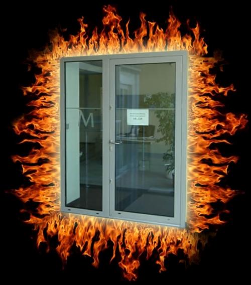 Szare, dwuskrzydłowe drzwi przeciwpożarowe z szybami, otoczone cyfrowo dodanym efektem płomieni na czarnym tle.