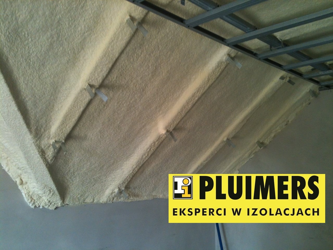 Ocieplenie poddasza pianką PUR, widoczne metalowe profile konstrukcyjne i logo firmy Pluimers.