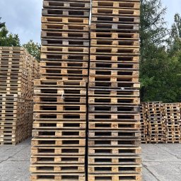 Palety Malicki - Stosy drewnianych palet EPAL ułożone na betonowym placu, z zielenią drzew w tle. Widoczne oznaczenia EPAL na paletach. Ujęcie z perspektywy żabiej.