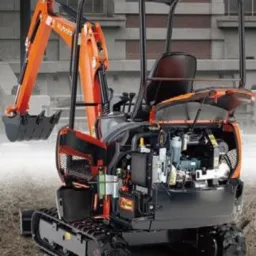 Pomarańczowo-czarna minikoparka Kubota KX016-4G z otwartą maską silnika, widoczny mechanizm, na ziemi, w tle budynek.