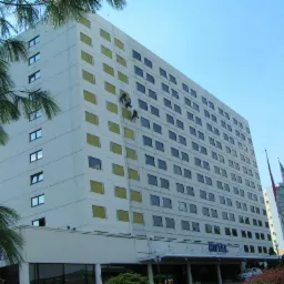 Dwaj alpiniści przemysłowi na linach, pracują na wysokościach przy elewacji wysokiego budynku hotelowego z licznymi oknami, zabezpieczonymi folią.