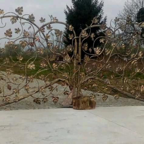 Dekoracyjna, metalowa brama ogrodowa z motywem winorośli, liści i winogron, z widocznymi elementami montażowymi u podstawy.