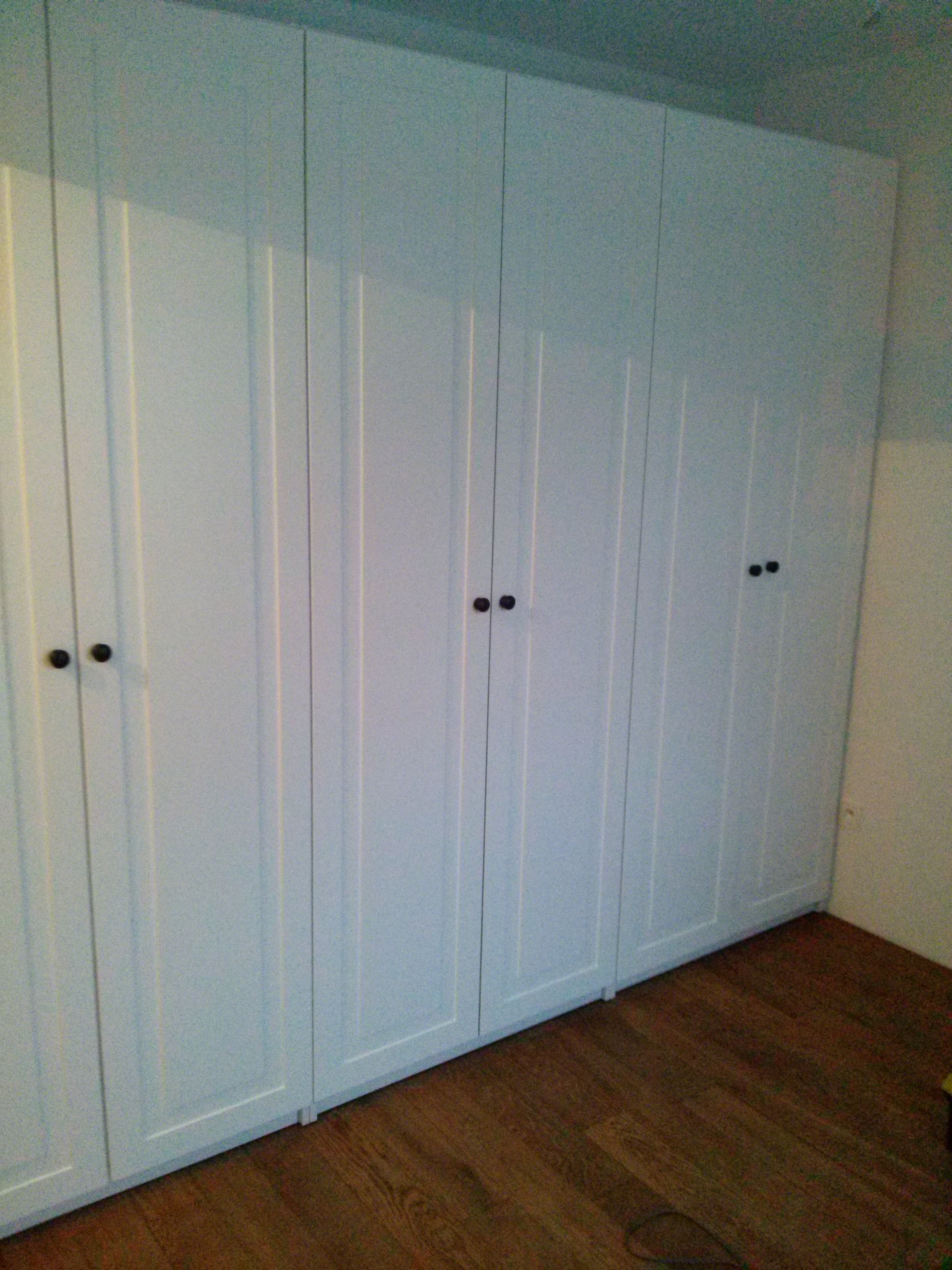 Biała szafa wnękowa z ciemnymi uchwytami na tle drewnianej podłogi, widok z dołu, podkreślający wysokość zabudowy.