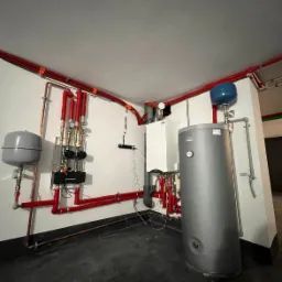 Instalacja centralnego ogrzewania z kotłem, zasobnikiem ciepłej wody i rozdzielaczem, rury miedziane i czerwone, widok na kotłownię