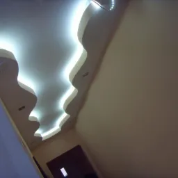 Dekoracyjny sufit podwieszany z oświetleniem LED w kształcie fal, widok z dołu, w tle fragment drzwi.