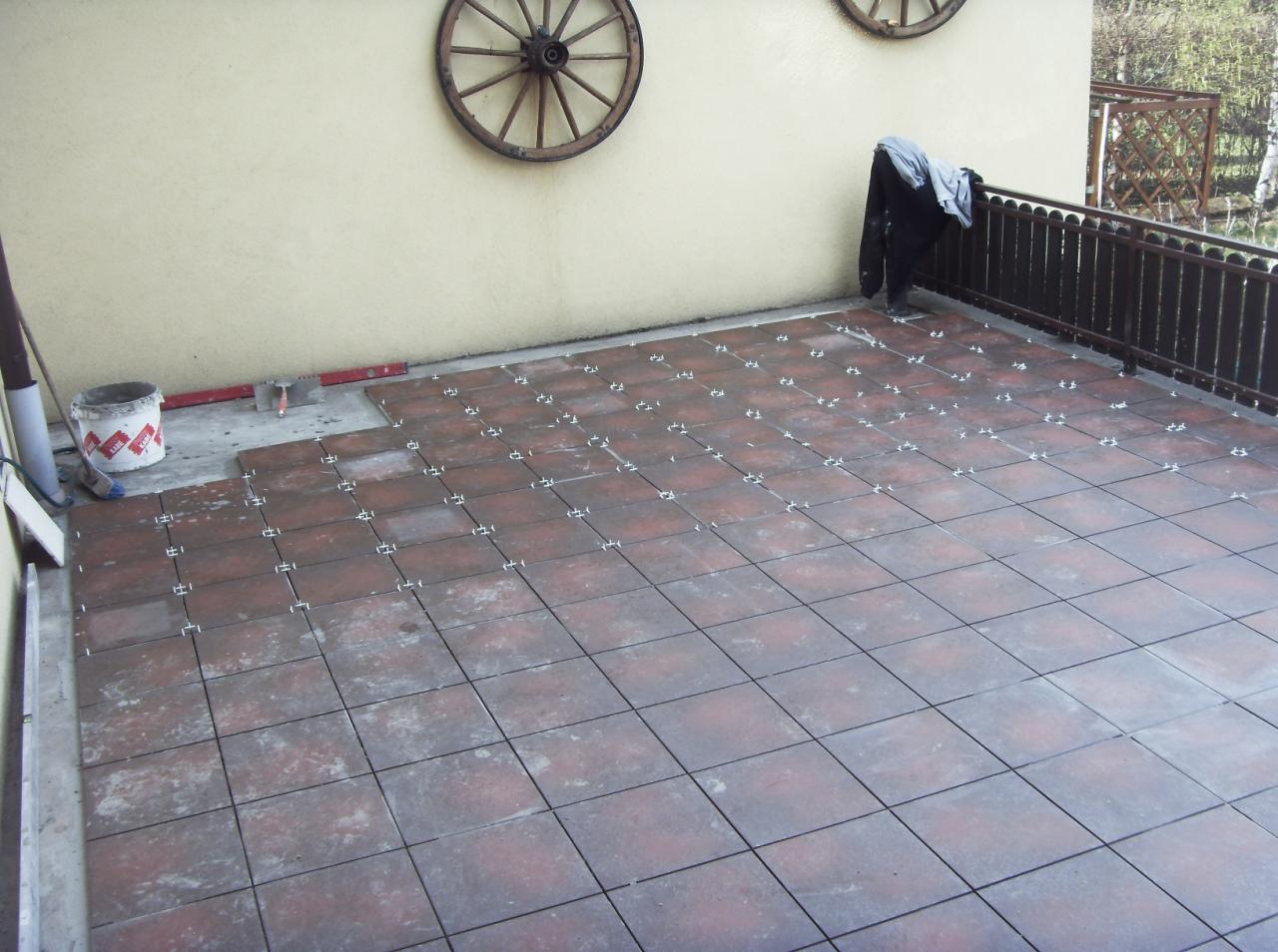 Montaż płytek tarasowych z użyciem krzyżyków dystansowych, widoczny fragment niezakończonej powierzchni i narzędzia glazurnicze.