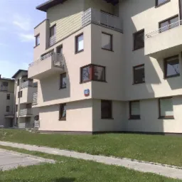 Nowoczesny budynek wielorodzinny z balkonami, elewacja w kolorze jasnego beżu, widoczny numer budynku 103, trawnik przed budynkiem.