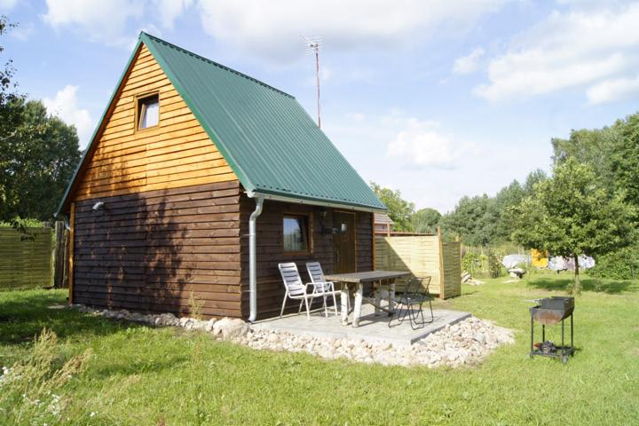 Niewielki, parterowy dom z drewna z zielonym dachem z blachy falistej, na posesji z trawnikiem, z widocznym stołem ogrodowym i grillem.