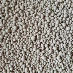 Beżowe granulki nawozu mineralnego, widoczne z góry, wypełniające całą powierzchnię kadru.