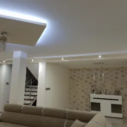 Salon z nowoczesnym oświetleniem sufitowym LED, wiszącą lampą o spiralnym kloszu i punktowymi reflektorami, widok na schody z metalową balustradą.