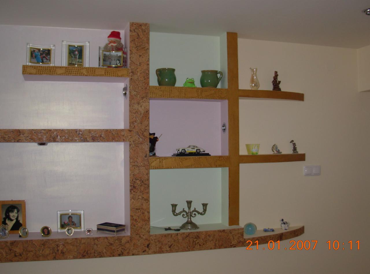 Nietypowe półki ścienne z płyty korkowej i drewnianych belek, zawierające dekoracyjne przedmioty, w tym ramki ze zdjęciami, figurki i świecznik.