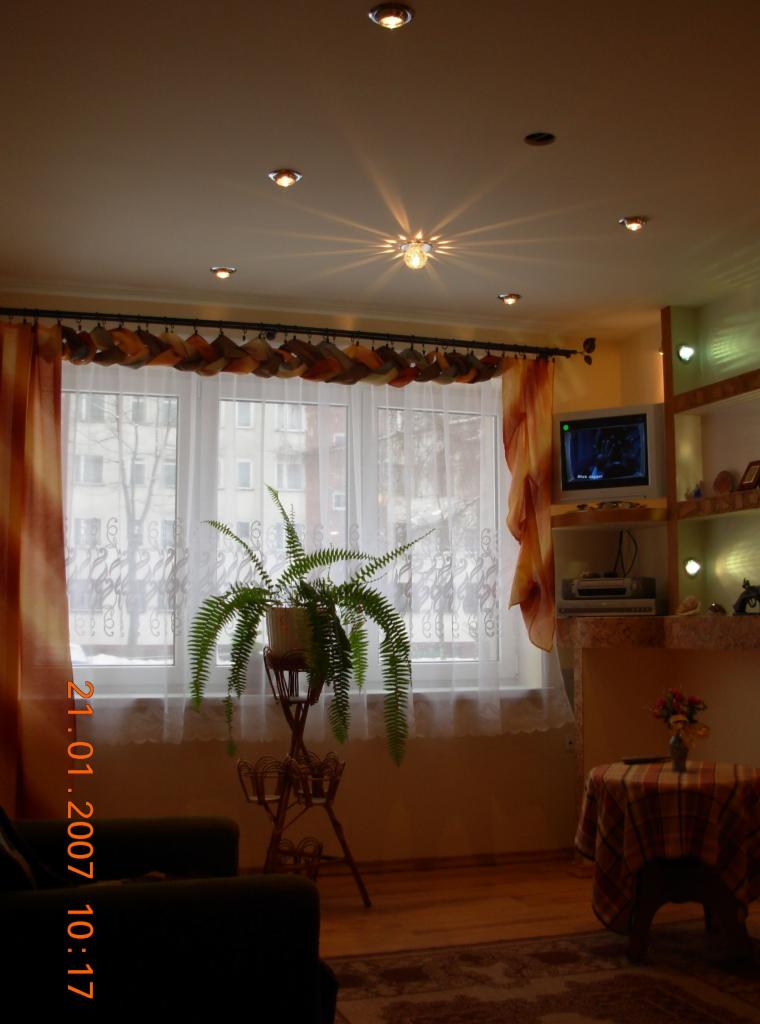 Salon z oświetleniem punktowym na suficie, zasłoniętym oknem i telewizorem w rogu, sfotografowany z niskiej perspektywy.