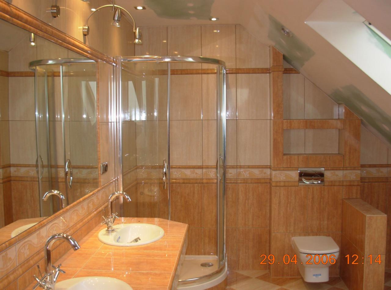 Beżowo-brązowa łazienka z kabiną prysznicową z zaokrąglonym szkłem, umywalką nablatową i toaletą. Widoczny fragment skośnego sufitu i data wykonania zdjęcia.