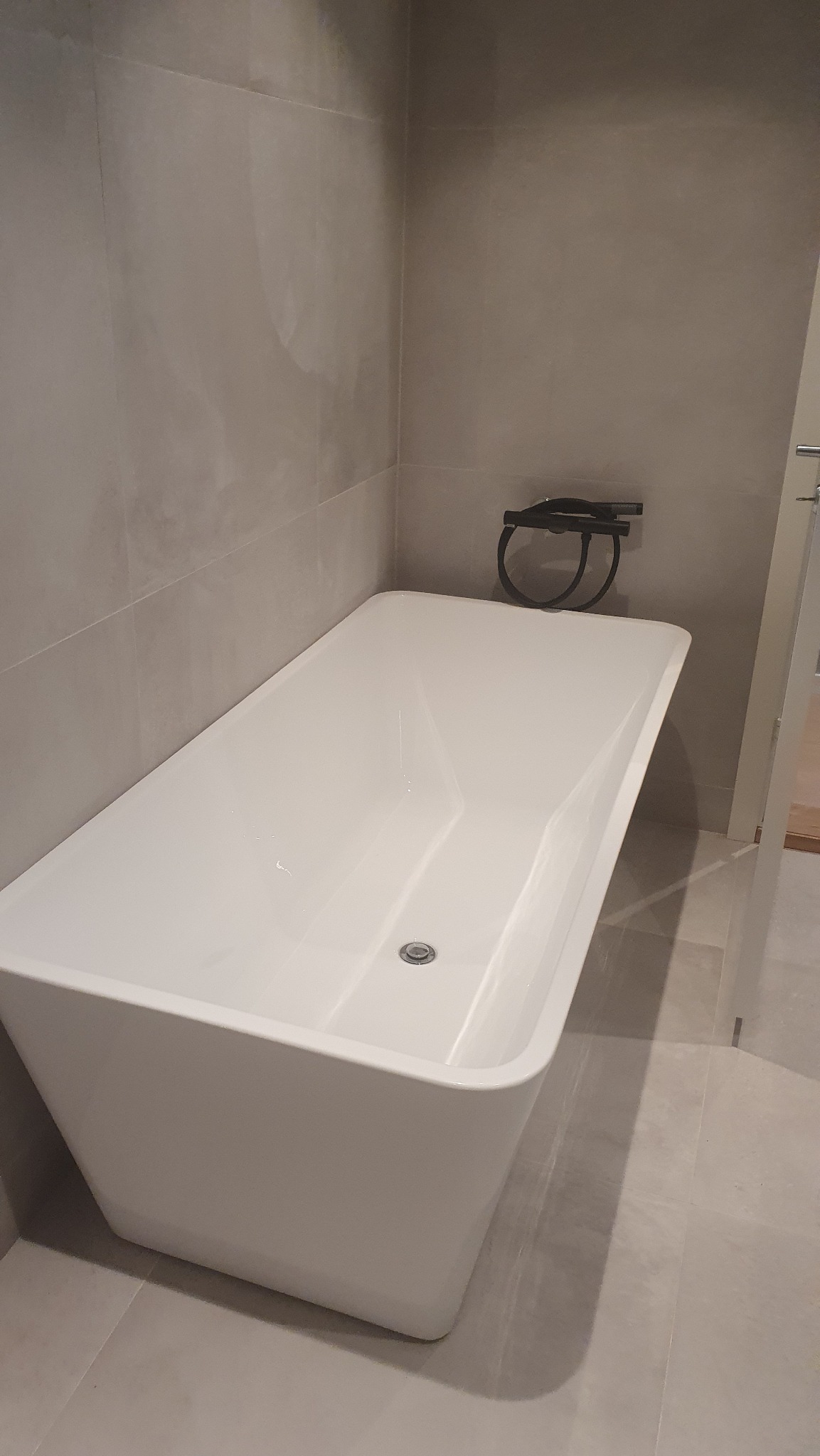 Nowoczesna, wolnostojąca wanna w minimalistycznej łazience z szarymi płytkami i czarną armaturą. Ujęcie z góry, podkreślające czystość i prostotę.