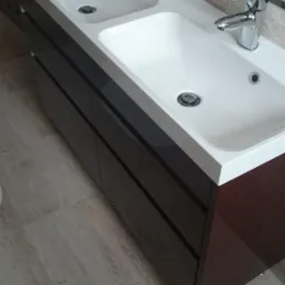 Nowoczesna szafka łazienkowa z dwoma umywalkami nablatowymi i lustrem. Ciemne, lakierowane fronty szafek kontrastują z jasnym blatem i płytkami podłogowymi.