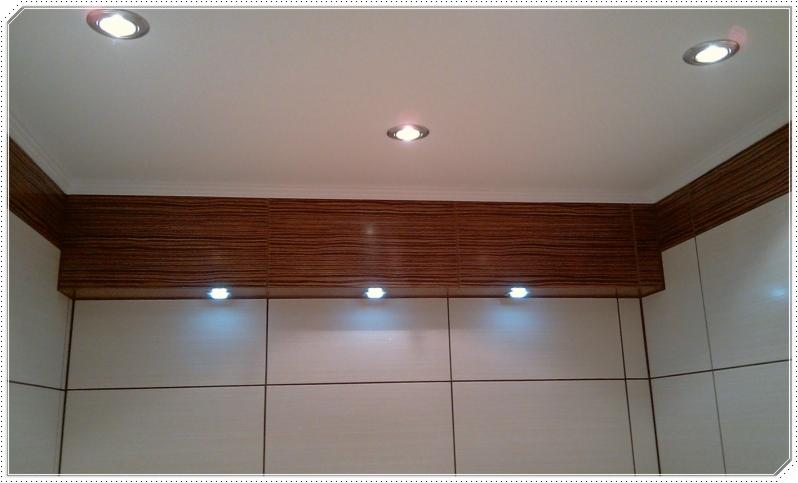 Wykończone wnętrze z podwieszanym sufitem, oświetleniem punktowym i panelami ściennymi w odcieniach bieli i brązu.