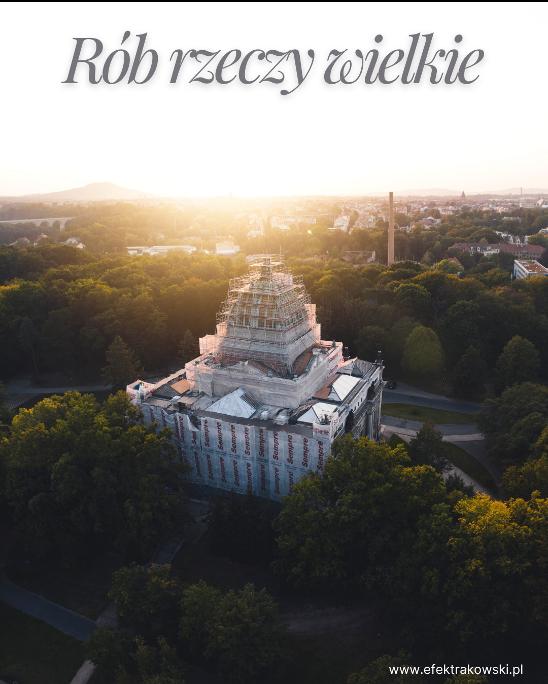 Renowacja zabytkowego budynku z rusztowaniem, otulonego folią ochronną z logo, widocznego z lotu ptaka na tle miejskiego krajobrazu o wschodzie słońca.