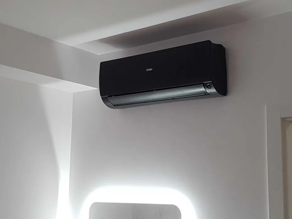 Czarny klimatyzator Haier zamontowany na białej ścianie w nowoczesnym wnętrzu. Widoczne oświetlenie LED w tle, podkreślające minimalistyczny design.