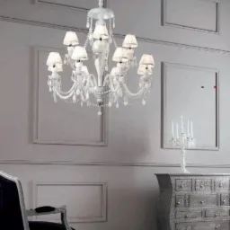 Elegancki, biały żyrandol kryształowy z abażurami w klasycznym wnętrzu z szarą komodą i krzesłem. Dekoracyjne listwy ścienne.