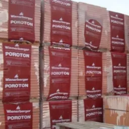 Sztaple palet z pustakami ceramicznymi Poroton Wienerberger, owinięte folią ochronną, składowane na placu budowy.