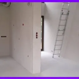 Wnętrze po nałożeniu tynków cementowo-wapiennych, widoczne gładkie ściany przygotowane pod malowanie, instalacje elektryczne wyprowadzone, aluminiowa drabina oparta o ścianę.