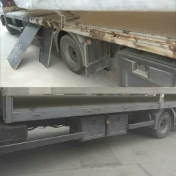 Dwu-częściowe ujęcie podwozia ciężarówki. Górna część pokazuje skorodowaną ramę i koło, z rampą dostępową. Dolna część prezentuje skrzynki narzędziowe i fragment ramy.