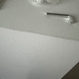 Merbud - Akcesoria montażowe do mebli: klucz imbusowy, wkręty w folii, śrubokręt z czerwoną rączką leżą na białym blacie szafki.