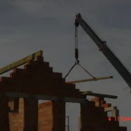 Budowa domu z cegły: dźwig podnosi drewniany element konstrukcyjny na szczyt ściany.