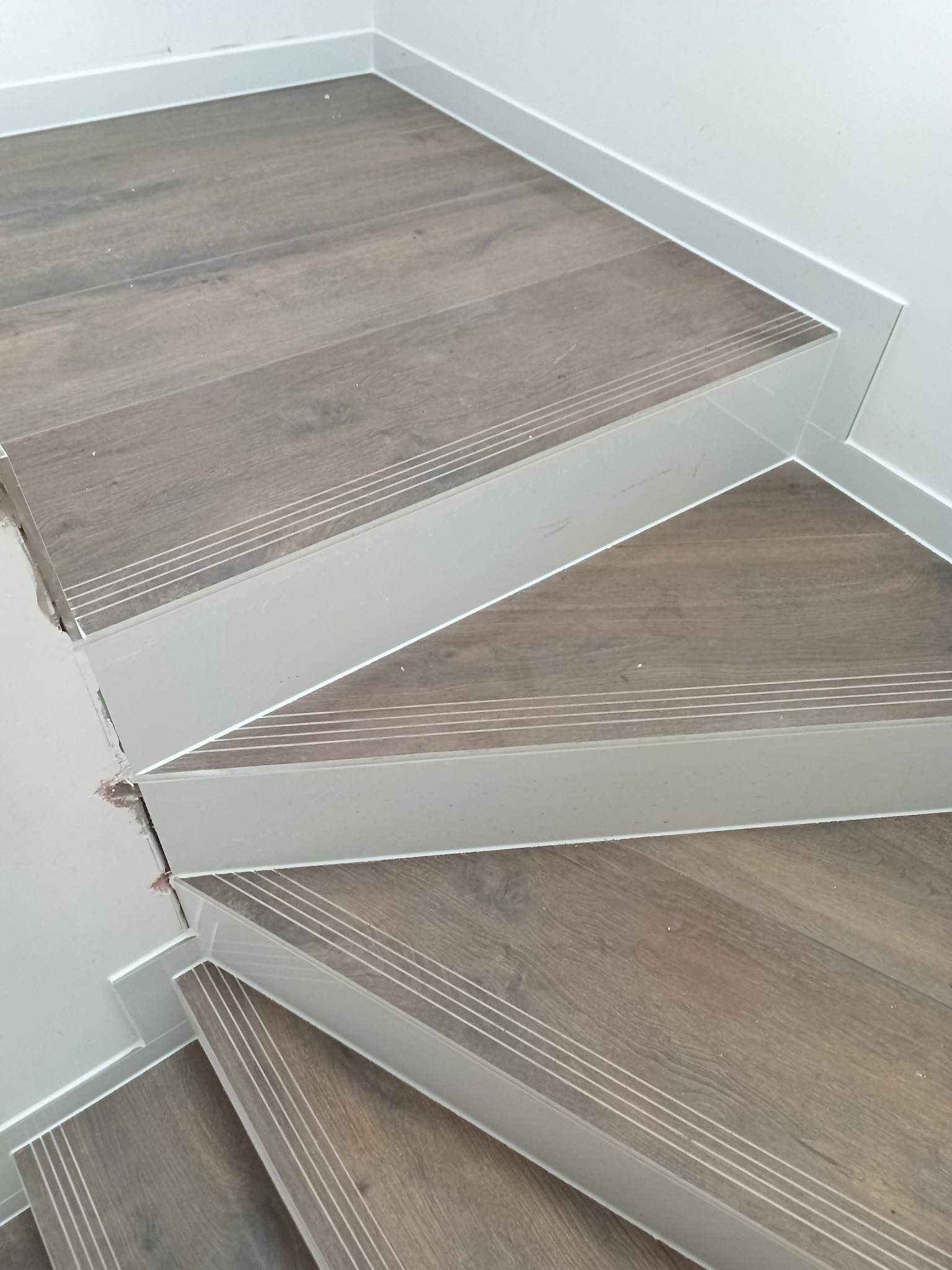 Drewnopodobne schody z białymi listwami antypoślizgowymi, widok z góry, fragment klatki schodowej po remoncie, detale wykończenia.