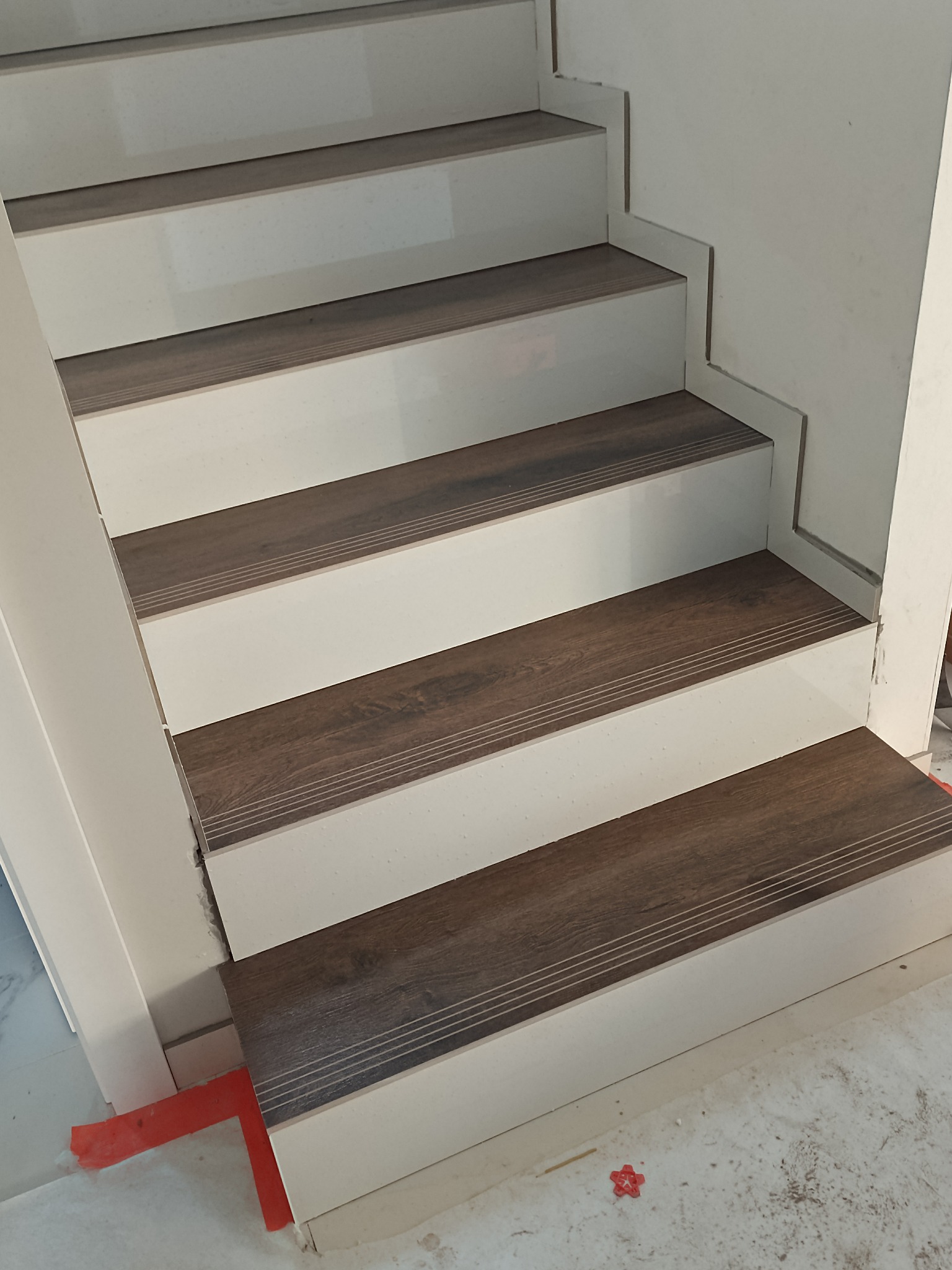 Schody z drewnopodobnymi nakładkami i białymi podstopnicami w Wieleniu. Wykończenie wnętrz z dbałością o detale, widoczne z bliska. Nowoczesny design.