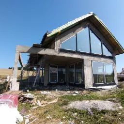 Dom w stanie surowym w Nowej Rudzie z zamontowanymi oknami o nietypowym kształcie, widoczne rusztowania i materiały budowlane.