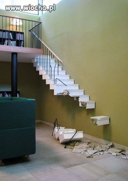 Uszkodzone, wiszące schody z oderwanymi stopniami i gruzem na podłodze, widok z dołu.