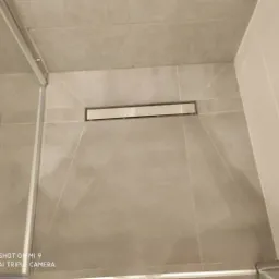 Szare płytki ceramiczne w kabinie prysznicowej z odpływem liniowym, widok z góry pod kątem.