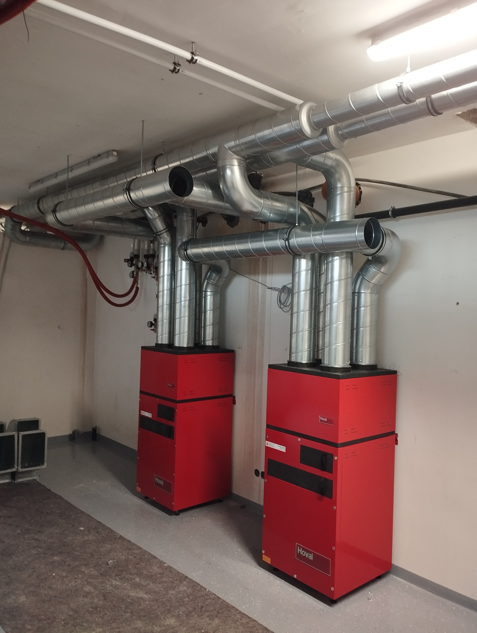 Dwa czerwone piece grzewcze marki Hoval z podłączonymi srebrnymi rurami wentylacyjnymi w piwnicy w Jarosławiu.