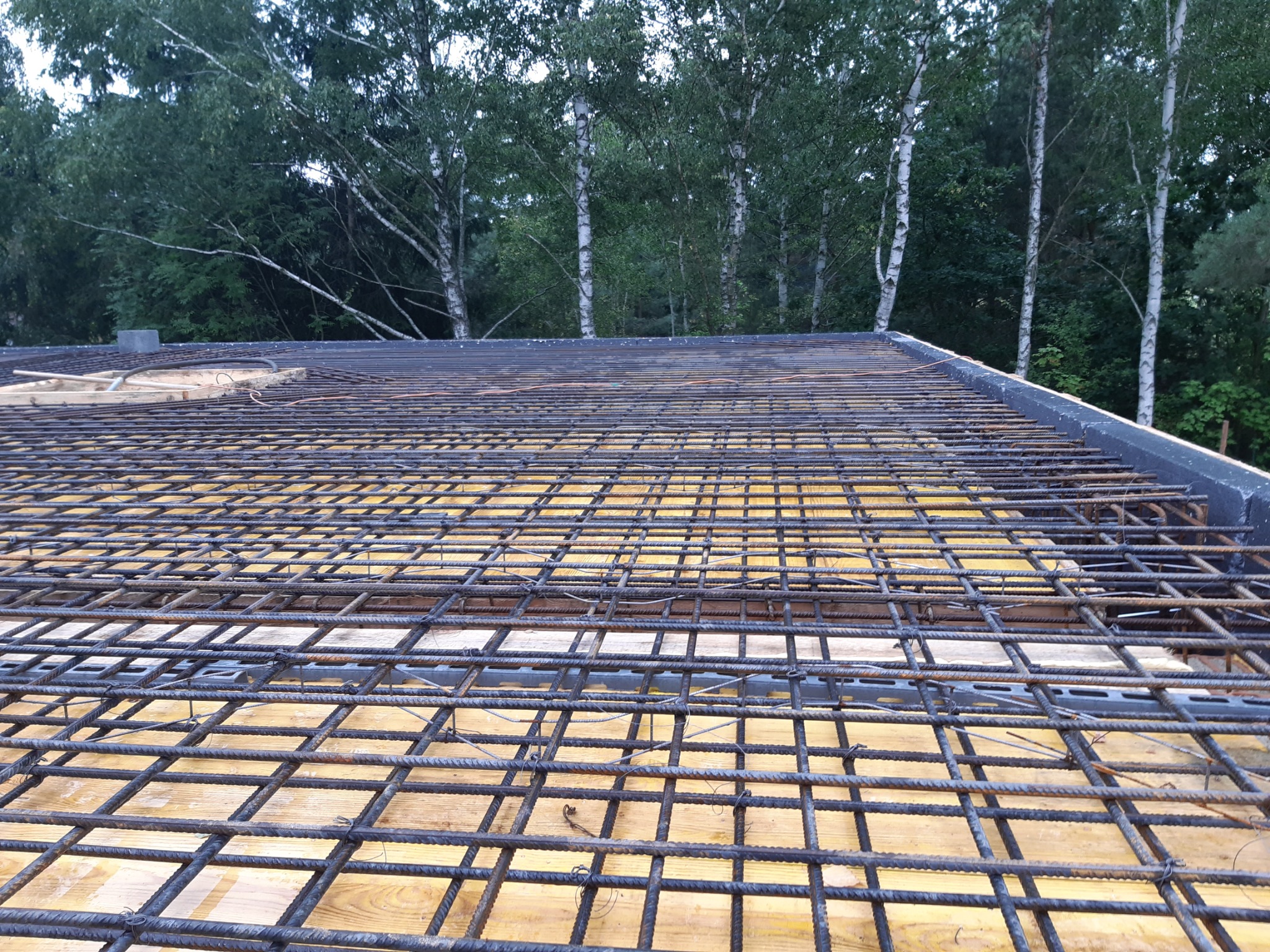 Zbrojenie stropu na deskowaniu, widok z góry na siatkę z prętów stalowych, w tle drzewa.