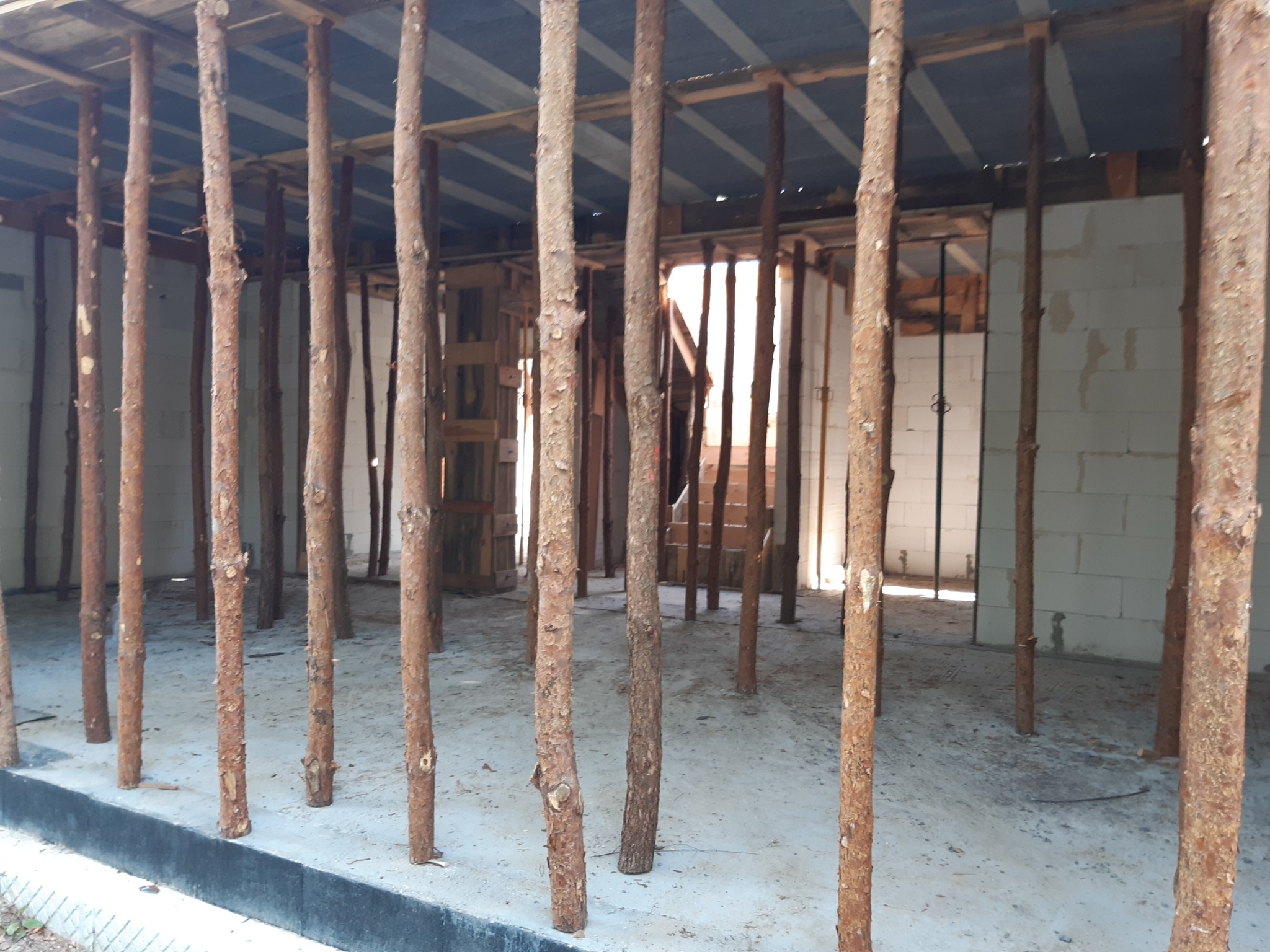 Wnętrze w trakcie budowy z widocznymi ścianami z bloczków i drewnianymi stemplami podtrzymującymi strop.