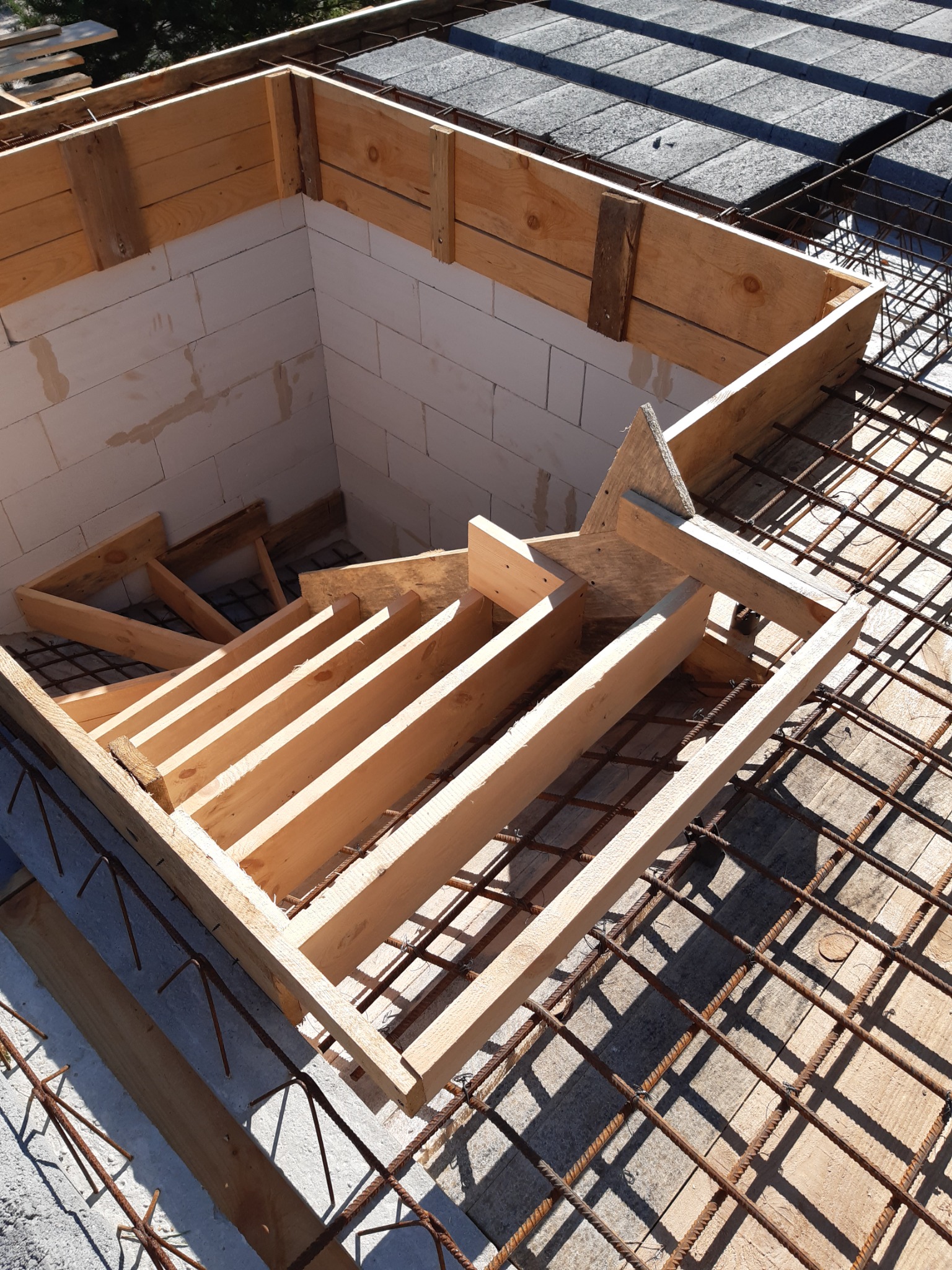 Szczegółowe ujęcie szalunku schodów wewnątrz konstrukcji budynku z betonu komórkowego, widoczna siatka zbrojeniowa i fragment pokrycia dachowego z papy.