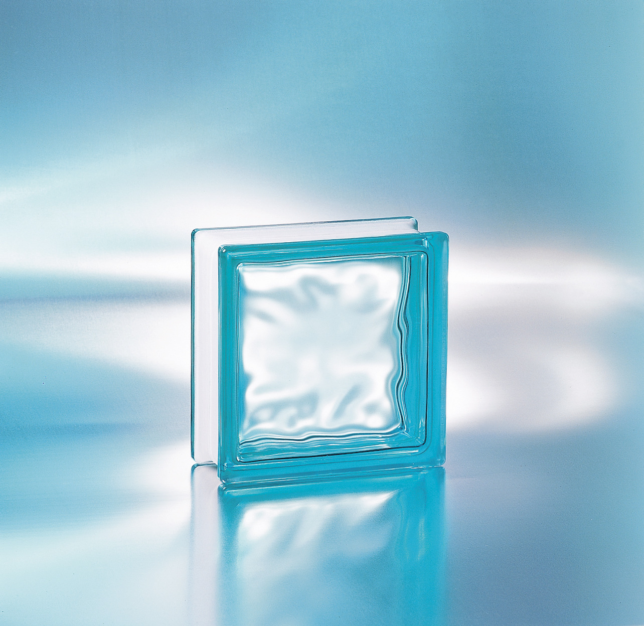 Szklany pustak w odcieniach błękitu, z wyraźną fakturą wewnętrzną, odbity w błyszczącym podłożu.