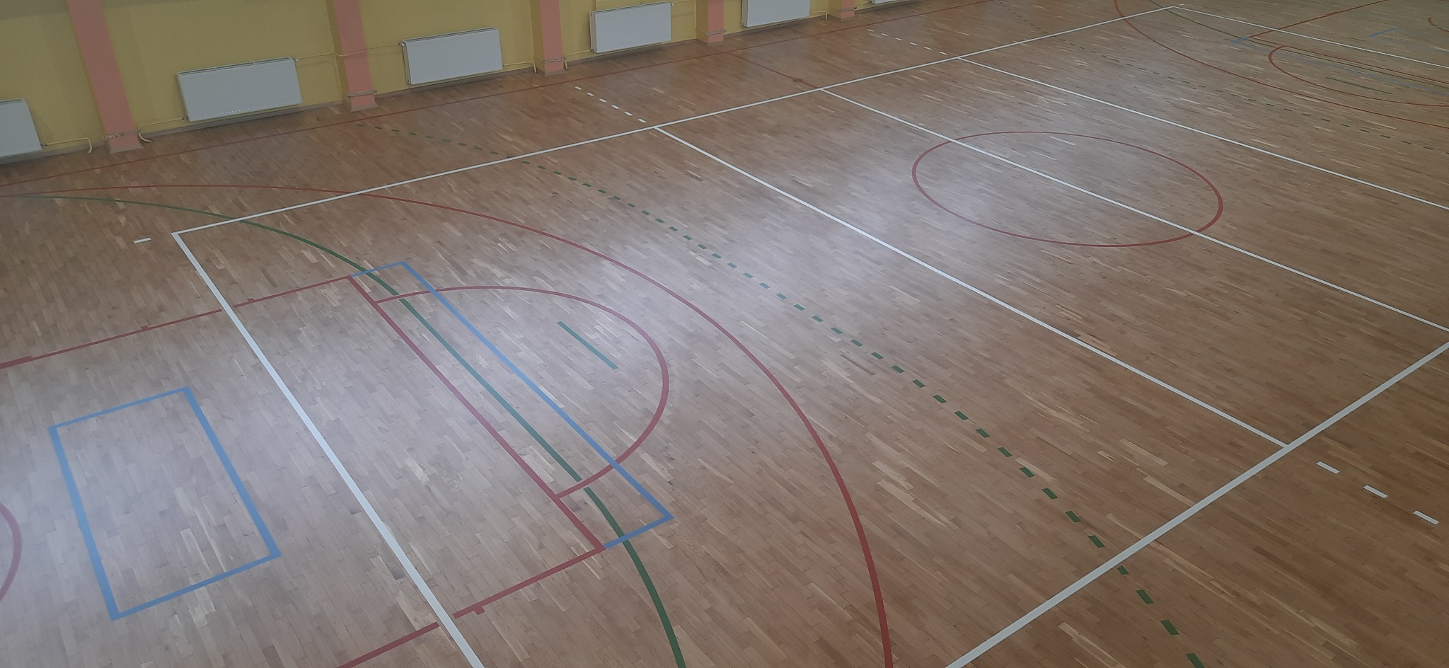 Parkietowa podłoga hali sportowej z liniami boisk do różnych gier, widok z góry.