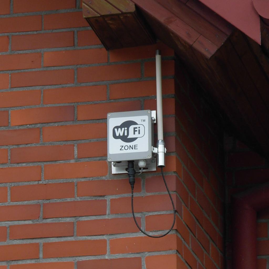 Zewnętrzna instalacja punktu dostępowego Wi-Fi Zone na ceglanej ścianie budynku z widoczną anteną i okablowaniem.
