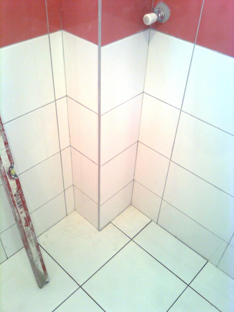 Wykończony narożnik łazienki z białymi i czerwonymi płytkami, widoczna poziomica przy ścianie, armatura na górze.