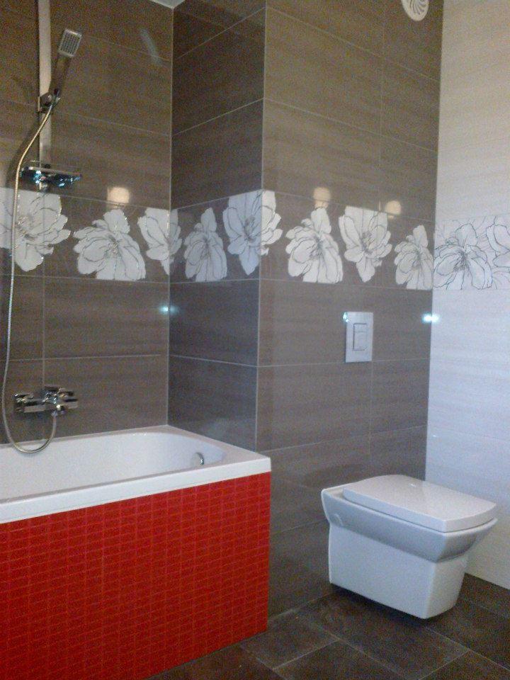 Wykończona łazienka w szaro-biało-czerwonej kolorystyce, z kwiatowym motywem na brązowych płytkach, widoczna wanna z czerwoną obudową, toaleta i kabina prysznicowa.