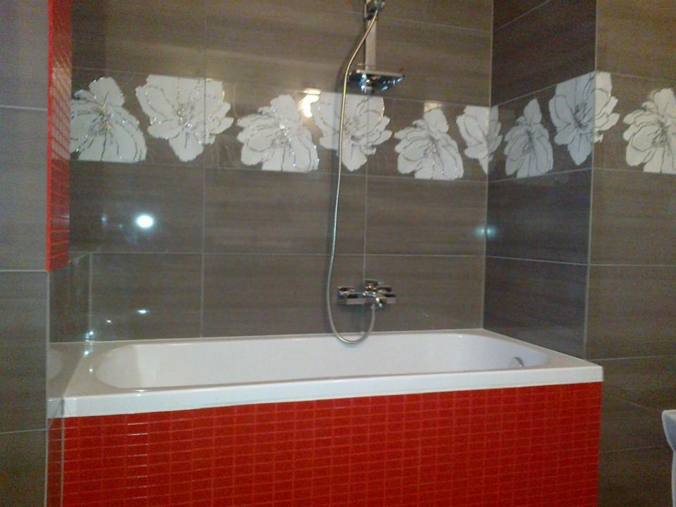 Wykończona łazienka z wanną obłożoną czerwoną mozaiką, szare płytki z motywem kwiatowym na ścianach i chromowana armatura.