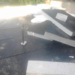 Izolacja termiczna dachu z papy: montaż płyt styropianowych na pokryciu z papy, widoczny kominek wentylacyjny i rozsypany piasek kwarcowy.