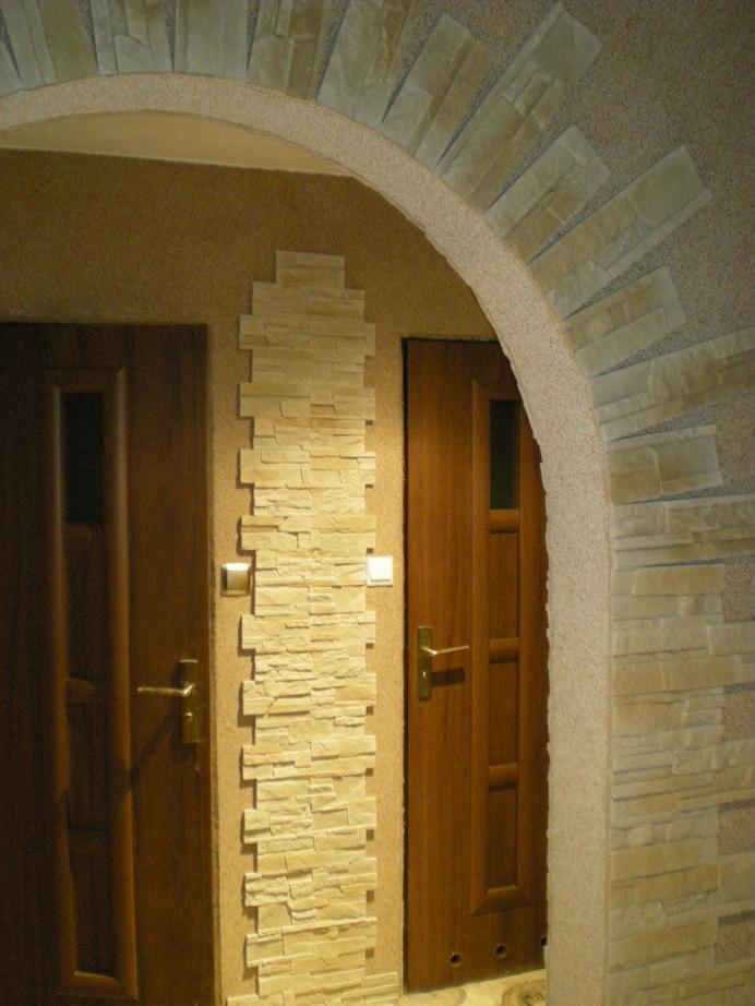 Aranżacja wnętrza z dwoma drewnianymi drzwiami, łukiem i pionowym panelem dekoracyjnym z kamienia elewacyjnego w odcieniach beżu i brązu.