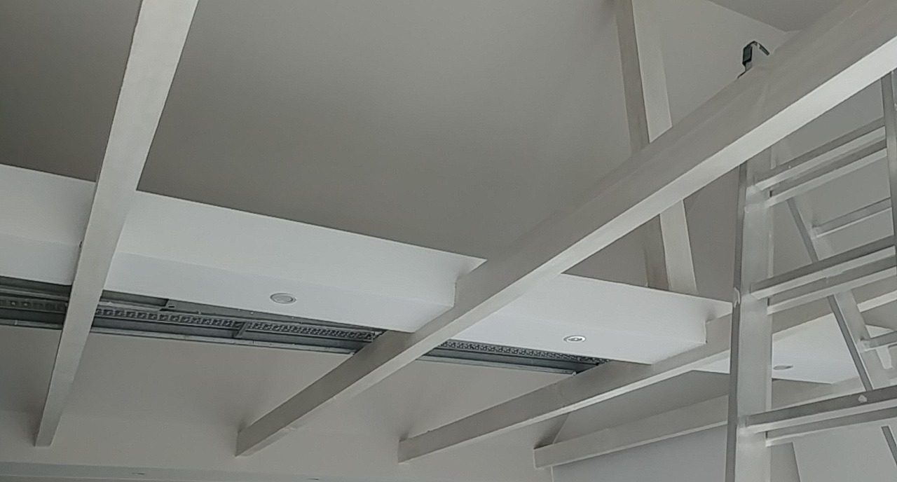 Sufit podwieszany z widocznymi profilami i oświetleniem punktowym, częściowo zakryty przez metalową drabinę.