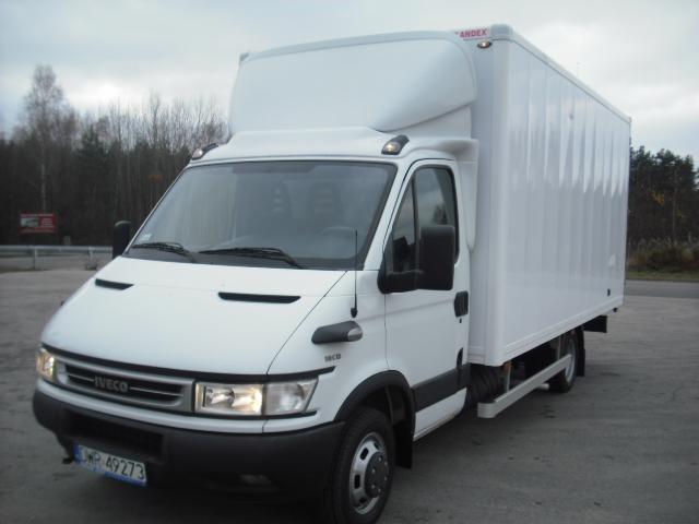 Biały samochód dostawczy Iveco 3.5T z zabudową kontenerową, zaparkowany na szarym asfalcie z widoczną tablicą rejestracyjną i lasem w tle.